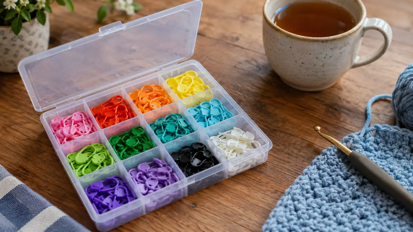 A small open storage box with rows of colorful locking stitch markers inside