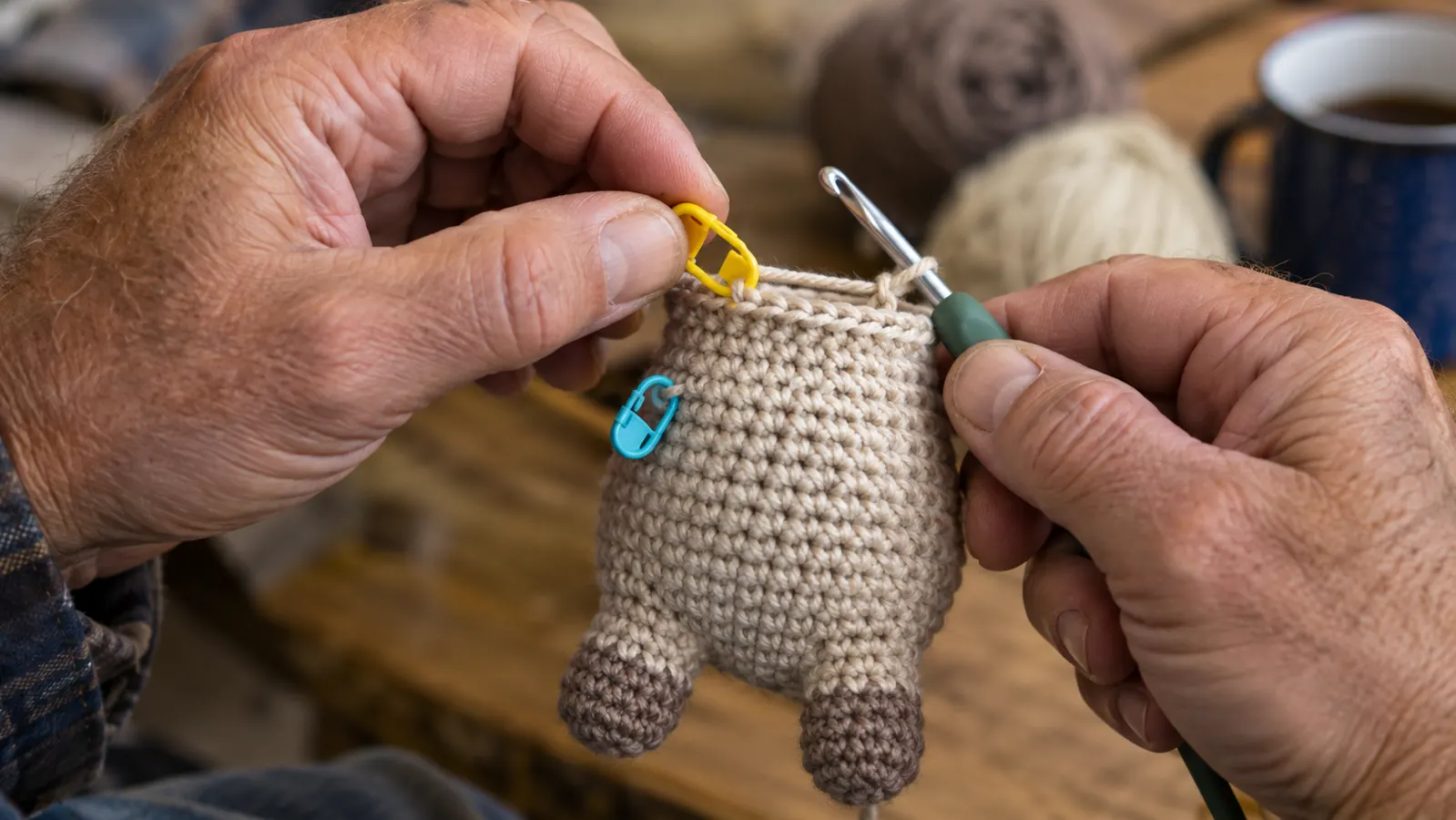 a crocheter's hands clipping a locking stitch marker over the first stitch of a new round on a small amigurumi body, yarn and hook in the other hand