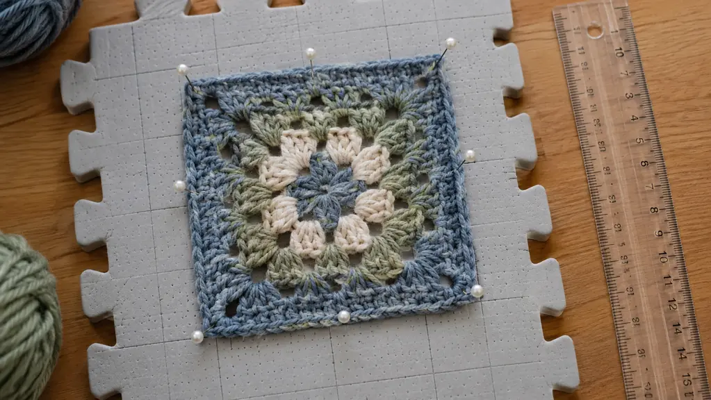 A crocheted square pinned into a perfect square on a blocking mat, with a ruler beside it